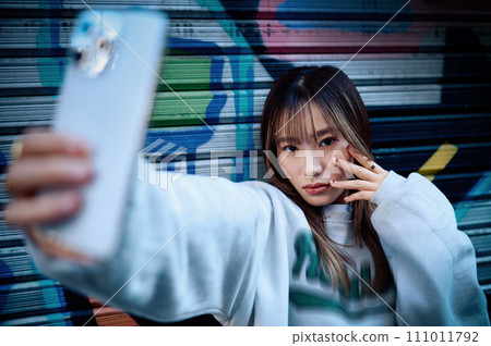 A young woman taking self photos with a smartphone 111011792