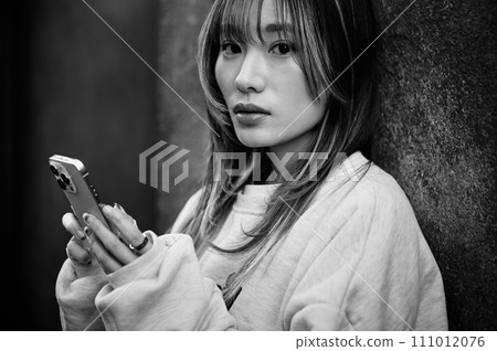 Young woman leaning against the wall and operating a smartphone Young woman leaning against the wall and operating a smartphone 111012076