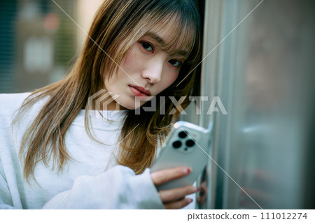 年輕女子靠在牆上操作智慧型手機 年輕女子靠在牆上操作智慧型手機 111012274