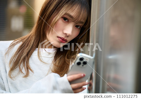 年輕女子靠在牆上操作智慧型手機 年輕女子靠在牆上操作智慧型手機 111012275