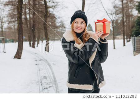 Cheerful blonde girl holding gift boxes on the park background. 30s female relaxing outdoors, winter time. Sale, shopping, holidays banner 111012298