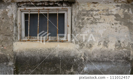 lattice window on a shabby dirty wall as a rough gloomy texture background, part of the wall of a terrible building with a window with iron bars, window to a basement or prison cell 111012457