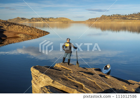 male canoe paddler with a paddle on a rocky shore of a mountain lake - Horsetooth Reservoir in northern Colorado in fall or winter scenery male canoe paddler with a paddle on a rocky shore of a mountain lake - Horsetooth Reservoir in northern Colorado in fall or winter scenery 111012586