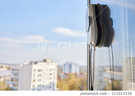 A window cleaner robot washes glass against the backdrop of multi-storey buildings. 111013338