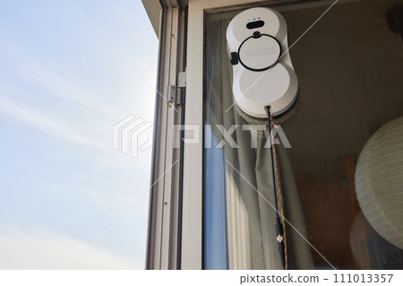 A window cleaner robot washes glass against the backdrop of multi-storey buildings. 111013357