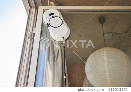 A window cleaner robot washes glass against the backdrop of multi-storey buildings. 111013361