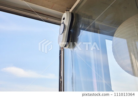 A window cleaner robot washes glass against the backdrop of multi-storey buildings. 111013364
