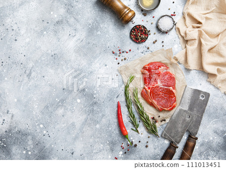 Fillet of raw beef rib eye steak on with meat cleaver,salt and pepper on light table Fillet of raw beef rib eye steak on with meat cleaver,salt and pepper on light table 111013451