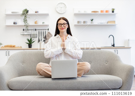 Female freelancer sitting on comfy couch in namaste pose. 111013619