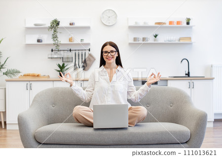 Woman sitting on couch with wireless laptop in front of her and meditating. Woman sitting on couch with wireless laptop in front of her and meditating. 111013621