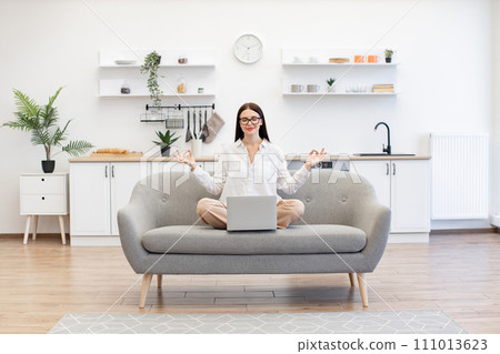 Woman meditating while working on portable laptop at living room. Woman meditating while working on portable laptop at living room. 111013623