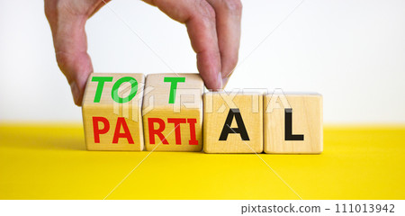Total or partial symbol. Businessman turns beautiful wooden cubes and changes the word Partial to Total. Beautiful yellow table white background. Business and total or partial concept. Copy space. Total or partial symbol. Businessman turns beautiful wooden cubes and changes the word Partial to Total. Beautiful yellow table white background. Business and total or partial concept. Copy space. 111013942