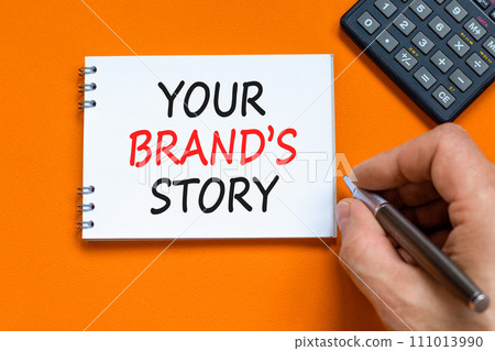 Branding and your brand story symbol. Concept words Your brands story on beautiful white note. Beautiful orange background. Businessman hand. Business branding your brand story concept. Copy space. Branding and your brand story symbol. Concept words Your brands story on beautiful white note. Beautiful orange background. Businessman hand. Business branding your brand story concept. Copy space. 111013990