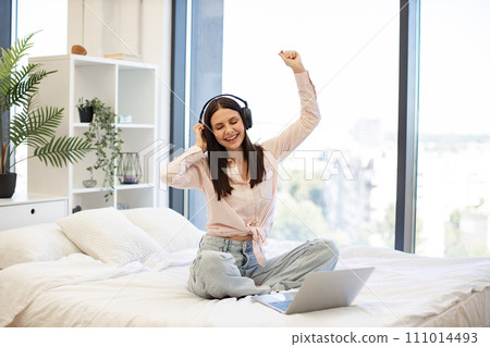 Woman relaxing on bed at home and using headphones for listening songs. Woman relaxing on bed at home and using headphones for listening songs. 111014493