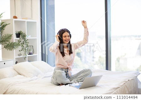 Woman relaxing on bed at home and using headphones for listening songs. Woman relaxing on bed at home and using headphones for listening songs. 111014494