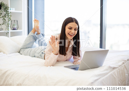 Brunette female waving hello while talking by video call using modern laptop. Brunette female waving hello while talking by video call using modern laptop. 111014536