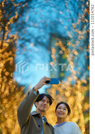 A man and a woman take a commemorative photo at a night view illuminated by illuminations 111014762