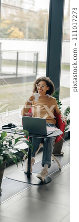 Smiling female freelancer have coffee break during working on laptop in modern coworking 111017273