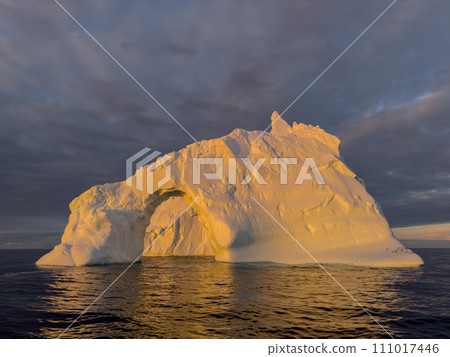 A huge high breakaway glacier drifts in the southern ocean off the coast of Antarctica at sunset, the Antarctic Peninsula, the Southern Arctic Circle, azure water, cloudy weather A huge high breakaway glacier drifts in the southern ocean off the coast of Antarctica at sunset, the Antarctic Peninsula, the Southern Arctic Circle, azure water, cloudy weather 111017446