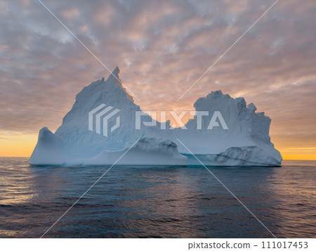 A huge high breakaway glacier drifts in the southern ocean off the coast of Antarctica at sunset, the Antarctic Peninsula, the Southern Arctic Circle, azure water, cloudy weather A huge high breakaway glacier drifts in the southern ocean off the coast of Antarctica at sunset, the Antarctic Peninsula, the Southern Arctic Circle, azure water, cloudy weather 111017453