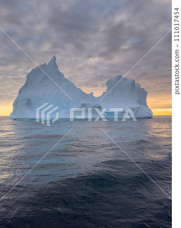 A huge high breakaway glacier drifts in the southern ocean off the coast of Antarctica at sunset, the Antarctic Peninsula, the Southern Arctic Circle, azure water, cloudy weather A huge high breakaway glacier drifts in the southern ocean off the coast of Antarctica at sunset, the Antarctic Peninsula, the Southern Arctic Circle, azure water, cloudy weather 111017454