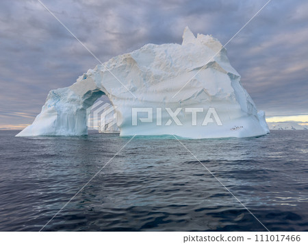 A huge high breakaway glacier drifts in the southern ocean off the coast of Antarctica at sunset, the Antarctic Peninsula, the Southern Arctic Circle, azure water, cloudy weather 111017466