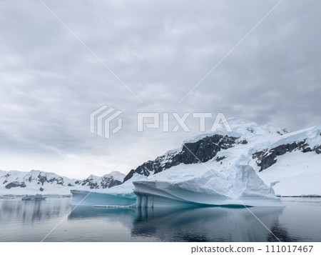 A huge high breakaway glacier in the southern ocean off the coast of Antarctica, the Antarctic Peninsula, the Southern Arctic Circle, azure water, cloudy weather 111017467