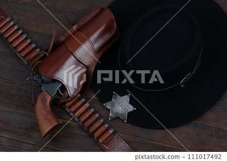 Sheriff star with gun, holster and gun belt with old west hat on table. Top view. Sheriff star with gun, holster and gun belt with old west hat on table. Top view. 111017492