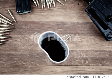 Cartridges and black coffee. Assault rifles with cartridges and cup of coffee on wooden table 111017498