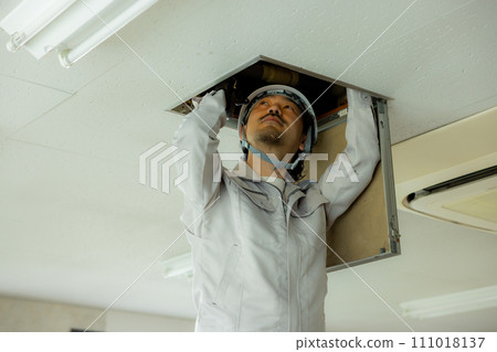 A man in work clothes inspecting the ceiling 111018137