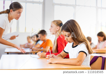 Interested preteen girl studying in classroom with classmates 111018585