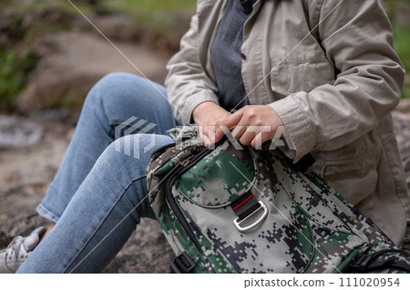 A woman finding something in her backpack while taking a break during her hiking trip. 111020954