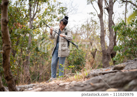 A positive Asian woman with a backpack is hiking on the mountain with a trekking pole. 111020976