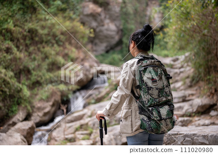 An adventure Asian woman with a backpack and a trekking pole is hiking on a rock mountain alone. 111020980