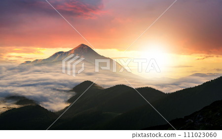 Sunset landscape with high peaks and foggy valley with thick white clouds under vibrant colorful evening sky in rocky mountains. Sunset landscape with high peaks and foggy valley with thick white clouds under vibrant colorful evening sky in rocky mountains. 111023060