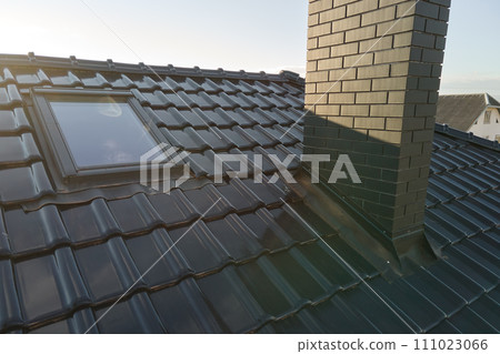 Closeup of attic window and brick chimney on house roof top covered with ceramic shingles. Tiled covering of building Closeup of attic window and brick chimney on house roof top covered with ceramic shingles. Tiled covering of building 111023066