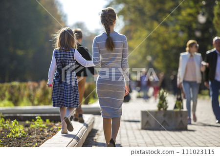 Back view of child girl and mother in dresses together holding hands on warm day outdoors on sunny background. 111023115