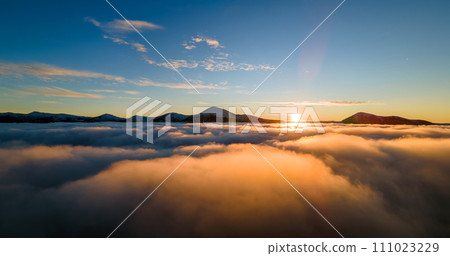 Aerial view of vibrant sunrise over white dense fog with distant dark Carpathian mountains on horizon. Aerial view of vibrant sunrise over white dense fog with distant dark Carpathian mountains on horizon. 111023229