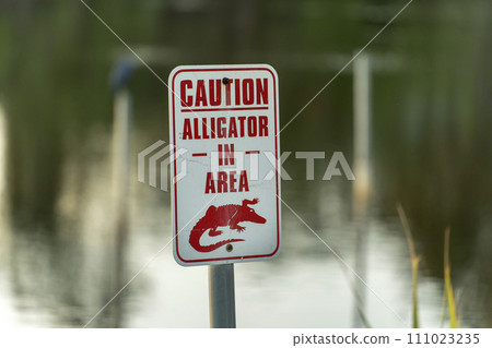 Alligator danger warning signpost in Florida waterfront park about caution and safety during walking near water Alligator danger warning signpost in Florida waterfront park about caution and safety during walking near water 111023235
