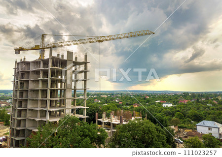 Aerial view of tower lifting crane and concrete frame of tall apartment residential building under construction in a city. Urban development and real estate growth concept. 111023257