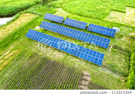 Blue solar photo voltaic panels mounted on metal frame standing on ground with green grass in field. 111023264