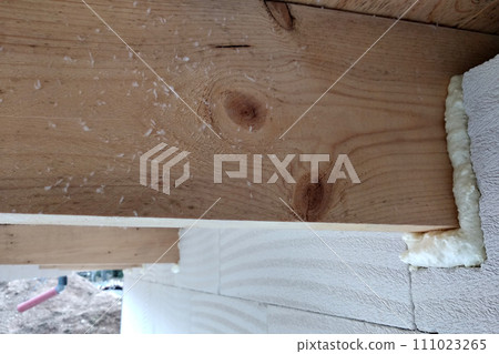 Installation of wooden beams of roof frame with spray foam on a house wall under construction. 111023265