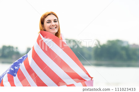 Back view of happy young woman with USA national flag on her shoulders. Positive girl celebrating United States independence day. 111023433