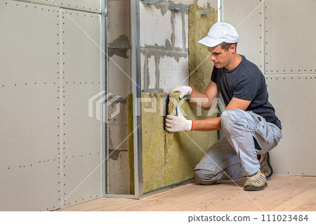 Worker insulating a room wall with mineral rock wool thermal insulation. 111023484
