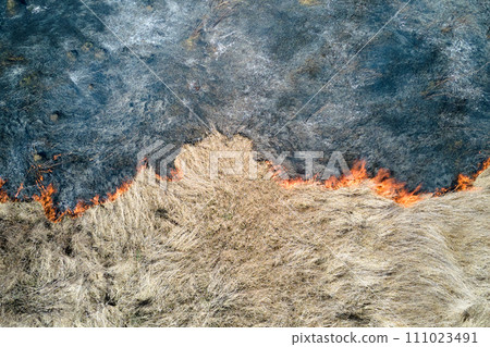 Aerial view of grassland field burning with red fire during dry season. Natural disaster and climate change concept Aerial view of grassland field burning with red fire during dry season. Natural disaster and climate change concept 111023491
