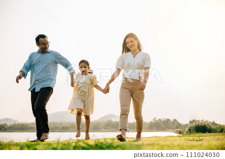 Father and mother with daughter walking together and smiling in a beautiful park on a sunny day, feeling the togetherness and the beauty of the outdoors, Happy family day 111024030