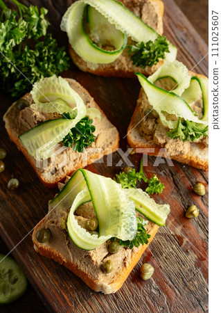 Open sandwiches with pate, cucumber, capers, and parsley on a old cutting board. 111025607