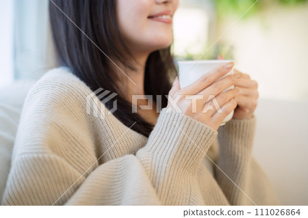 A woman drinking coffee while relaxing on a sofa A woman drinking coffee while relaxing on a sofa 111026864