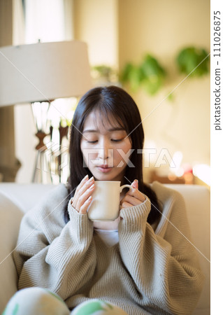 A woman drinking coffee while relaxing on a sofa 111026875