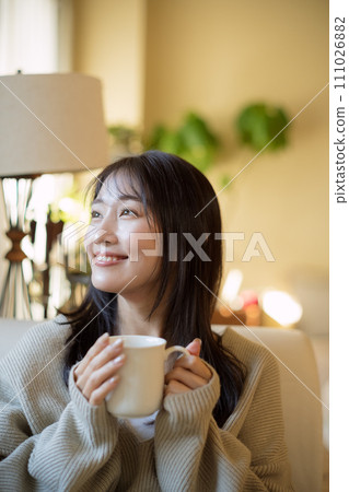 A woman drinking coffee while relaxing on a sofa A woman drinking coffee while relaxing on a sofa 111026882